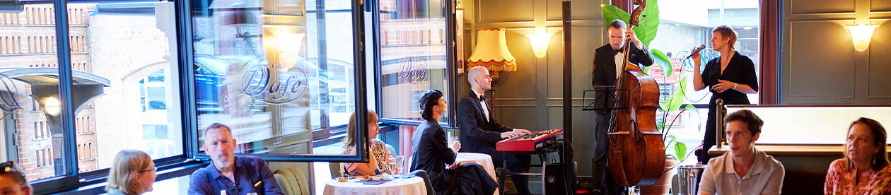 A jazz band playing at Café Duse, with several guest looking toward them. The windows are open